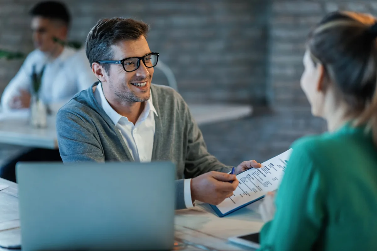 A smiling advisor going over a financing document with a customer across a table, with a laptop in the foreground
